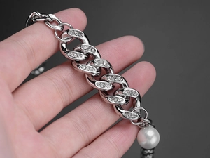 Close-up of silver Cuban link chain featuring set diamonds and a large white pearl drop