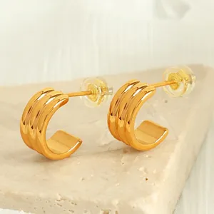 Boucles d'oreilles géométriques dorées en forme de C sur une surface en marbre naturel