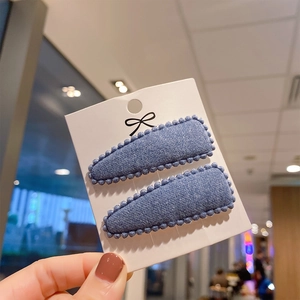 Close-up of two blue faux cashmere teardrop hair clips with beaded edges on a card