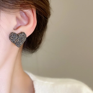 Gros plan de boucles d'oreilles cœur élégantes avec cristaux gris foncé sur l'oreille