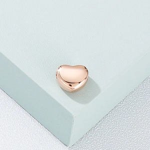 Minimalist heart pendant in rose gold finish on a geometric stand with metallic texture