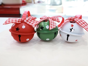Three metal Christmas bells with star cutouts and festive plaid bows on a beige surface