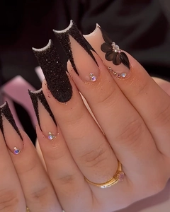 Detail of matte black press-on nails with 3D floral carvings and rhinestone accents