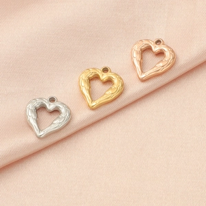 Three textured heart charms in silver, gold, and rose gold on pink silk fabric