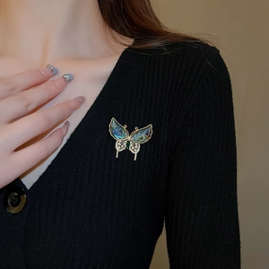 Détail d'une broche papillon en nacre et zircons portée sur un cardigan noir élégant