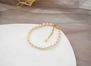 Detail view of handmade freshwater pearl bracelet with gold beads on white ceramic plate