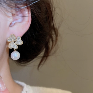 Close-up of floral gold earrings with sparkling zircon petals and elegant drop pearls