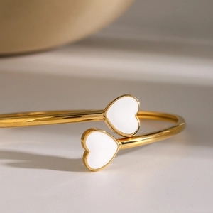 Macro view of gold-plated stainless steel cuff featuring white enamel hearts