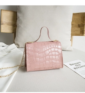 Pink crocodile pattern handbag with gold chain strap on a soft grey sofa setting