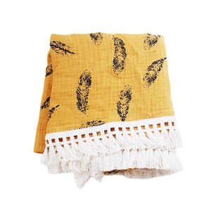 Yellow muslin baby blanket with black feather prints and white fringe trim, folded view