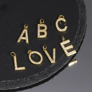 Close-up of golden letter pendants with cubic zirconia inlay on black stone surface