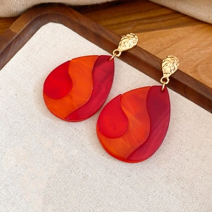 Detailed view of teardrop earrings with red wavy resin texture and gold hammered studs