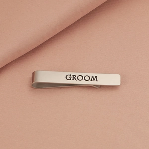 Detailed close-up of a silver stainless steel tie clip with black GROOM engraving on fabric