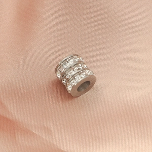 Macro shot of silver cylindrical spacer bead with square crystals on pink silk fabric