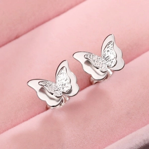 Macro shot of 3D layered silver butterfly studs with hammered texture on pink velvet