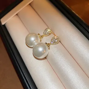 Elegant gold plated pearl drop earrings with zircon studs on a soft beige satin background