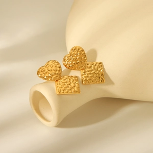 Gold plated square and heart textured stud earrings on beige ceramic dish