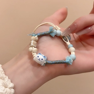 Close-up of handmade ceramic cat pendant on a woven bead bracelet in hand