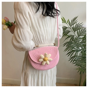 Close-up of a pink woven crossbody bag featuring a 3D white daisy and woven strap