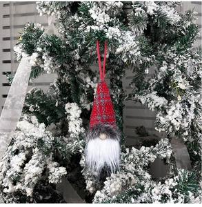 Detail of red plaid Swedish gnome ornament hanging on a snowy Christmas tree branch
