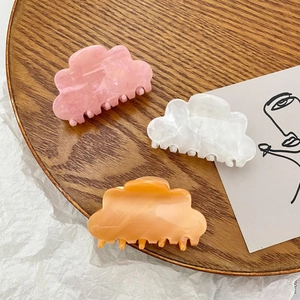 Cloud-shaped acrylic hair claws in pink, white, and orange on a wooden tray