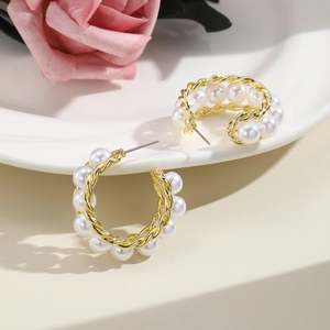 Elegant vintage C-shaped gold twist earrings with white pearls displayed on ceramic