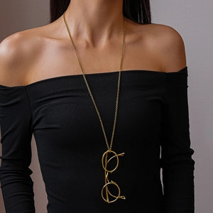 Close-up of a long golden necklace featuring a unique vintage eyewear frame pendant on a model