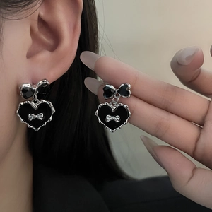 Détail de la boucle d'oreille nœud noir et cœur argenté portée avec accents métalliques