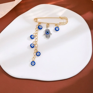 Gold Hamsa hand brooch with blue evil eye charms and tassels on a white ceramic tray