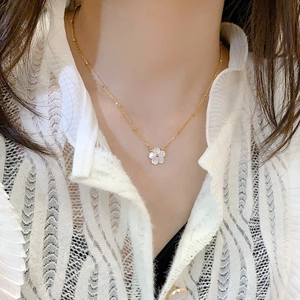 Close-up of a delicate gold bead chain necklace featuring a white shell cherry blossom pendant