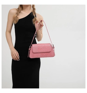 Detail view of a pink crocodile pattern handbag worn by a model in a black dress