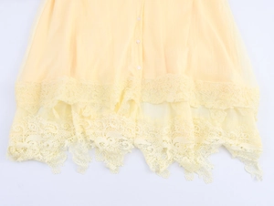 Détail d'ourlet de robe en mousseline jaune clair avec dentelle et boutons verticaux