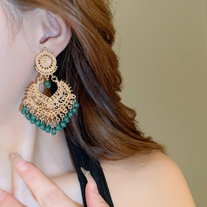 Close-up of ethnic hollow teardrop earrings with vintage gold finish and green beads
