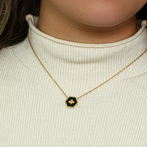 Close-up of golden necklace featuring a black hexagonal pendant with a gold bee motif