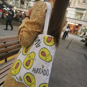White canvas tote bag featuring a cute avocado print shown in a street style lifestyle setting