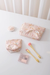 Detail of pink floral jacquard cosmetic bags with gold thread texture and brand label