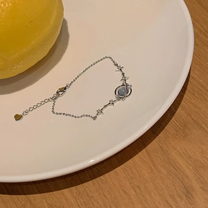 Detailed view of silver planet and star bracelet with blue stone on a ceramic plate