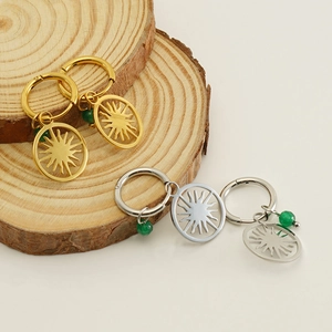 Hollow sun charm earrings with green beads in gold and silver finish on wooden base