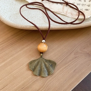 Close-up of bronze ginkgo leaf pendant with wooden bead on brown leather necklace cord