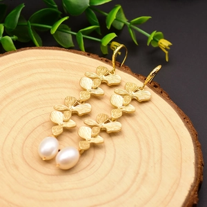 Floral gold-plated drop earrings with white pearls on a natural wood surface