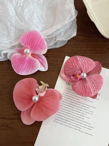 Detailed close-up of three gradient pink orchid hair clips with white pearl centers