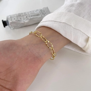 Detail of a gold irregular link chain bracelet worn on a wrist for a minimalist aesthetic