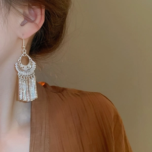 Close-up of silver hollow carved geometric tassel earrings on a model in vintage style