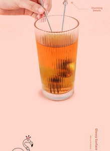 Close-up of ribbed glass cup with amber liquid and flamingo-topped metal stirrers