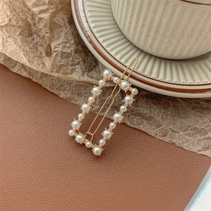 Close-up of golden rectangle hair clip with elegant white pearls on leather texture