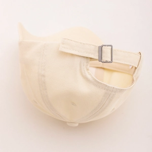 Detail of adjustable metal buckle and cotton twill strap on beige baseball cap