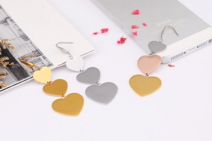 Detailed view of triple heart drop earrings in gold, silver, and rose gold finishes