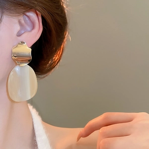 Close-up of irregular metal and cream oval drop earrings on model for elegant look