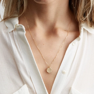 Layered beaded crystal necklace with golden hammered disc pendant worn on a model