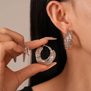 Vintage hollow silver hoop earrings featuring Greek meander pattern on a female model